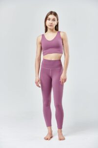A young woman modeling pink activewear, standing against a white backdrop.
